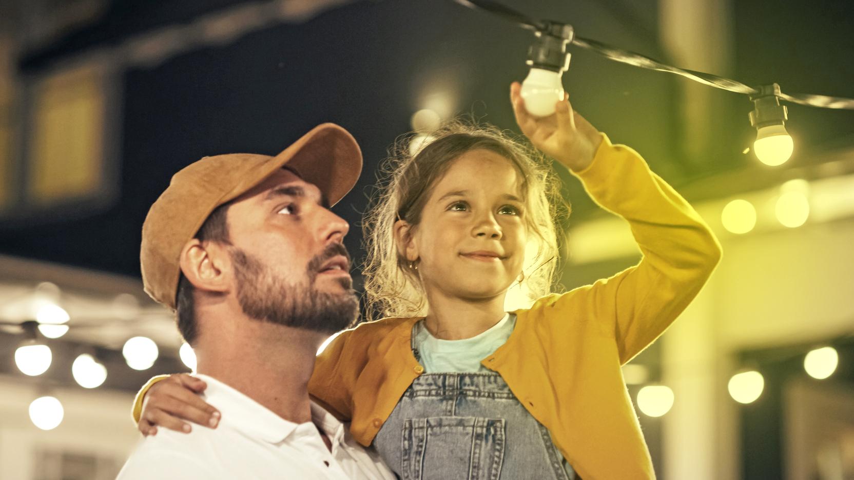 Ein Mann hat ein Mädchen auf dem Arm, das auf eine Lichterkette zeigt Ein Mann hat ein Mädchen auf dem Arm, das auf eine Lichterkette zeigt