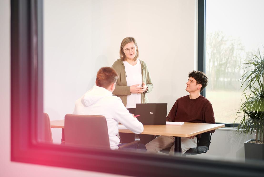 Drei junge Menschen sitzen an einem Besprechungstisch und arbeiten Drei junge Menschen sitzen an einem Besprechungstisch und arbeiten