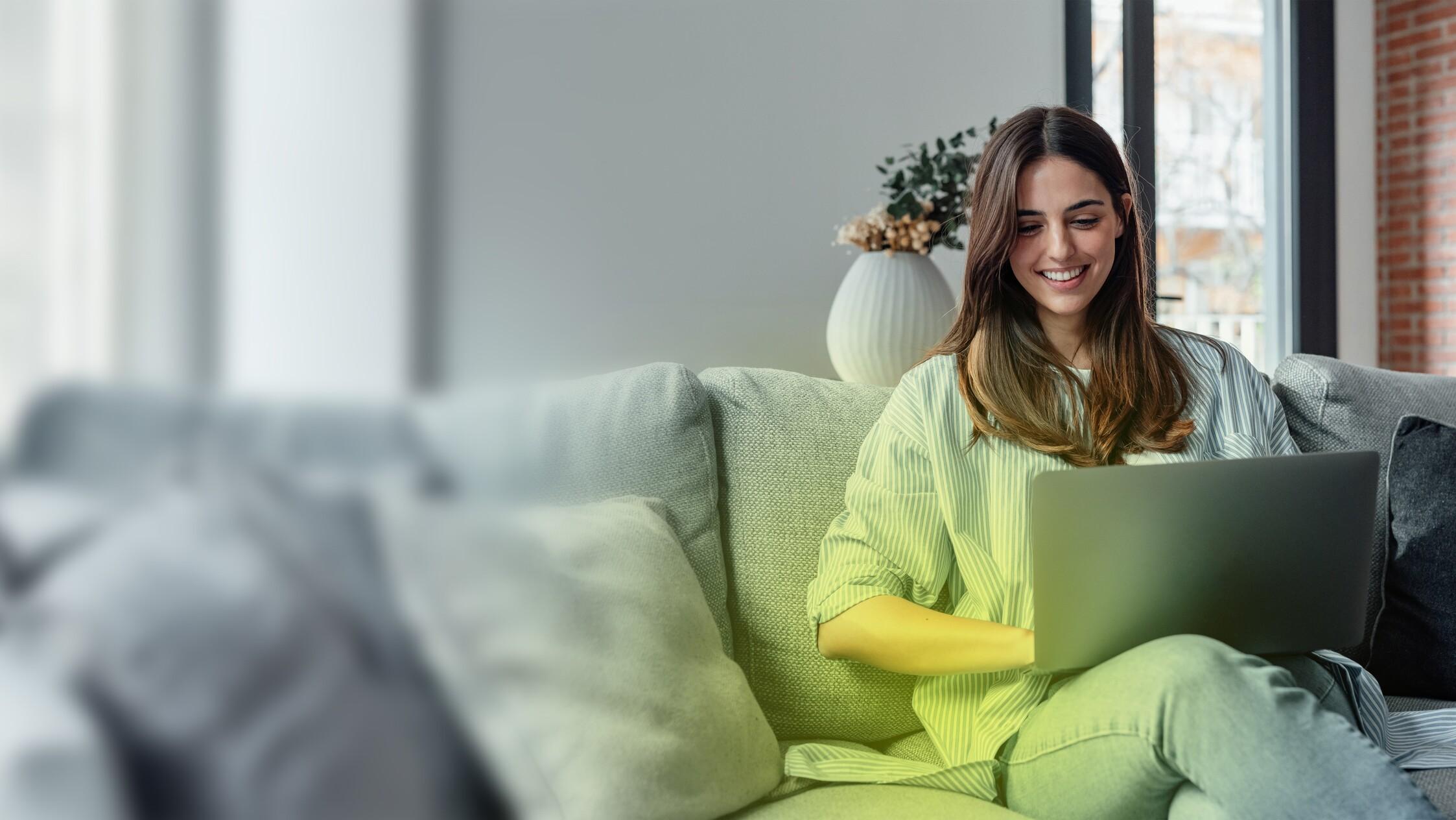 Eine junge Frau sitzt auf dem Sofa und hat einen Laptop auf dem Schoß Eine junge Frau sitzt auf dem Sofa und hat einen Laptop auf dem Schoß