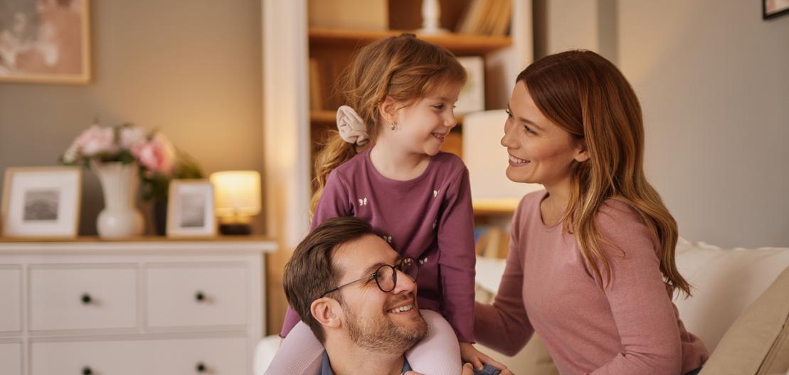 Eine Frau und ein Mann sitzen auf dem Sofa und kuscheln mit einem kleinen Mädchen Eine Frau und ein Mann sitzen auf dem Sofa und kuscheln mit einem kleinen Mädchen