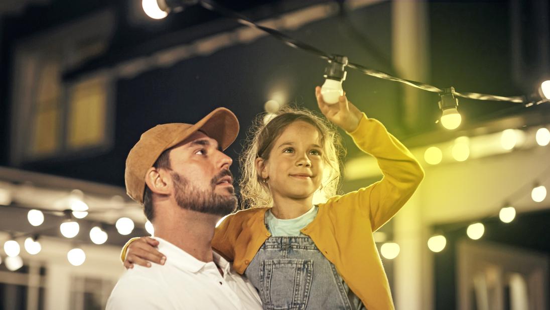 Ein Mann hat ein Mädchen auf dem Arm, das auf eine Lichterkette zeigt Ein Mann hat ein Mädchen auf dem Arm, das auf eine Lichterkette zeigt