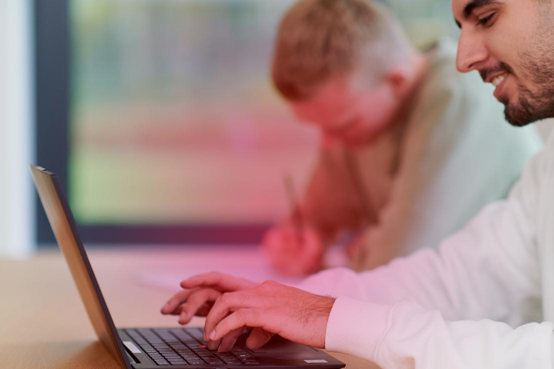 Zwei junge Männer sitzen an einem Schreibtisch und haben einen Laptop vor sich Zwei junge Männer sitzen an einem Schreibtisch und haben einen Laptop vor sich