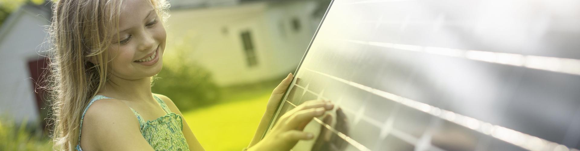 Ein Mädchen steht vor einem Photovoltaik-Modul und schaut es an Ein Mädchen steht vor einem Photovoltaik-Modul und schaut es an