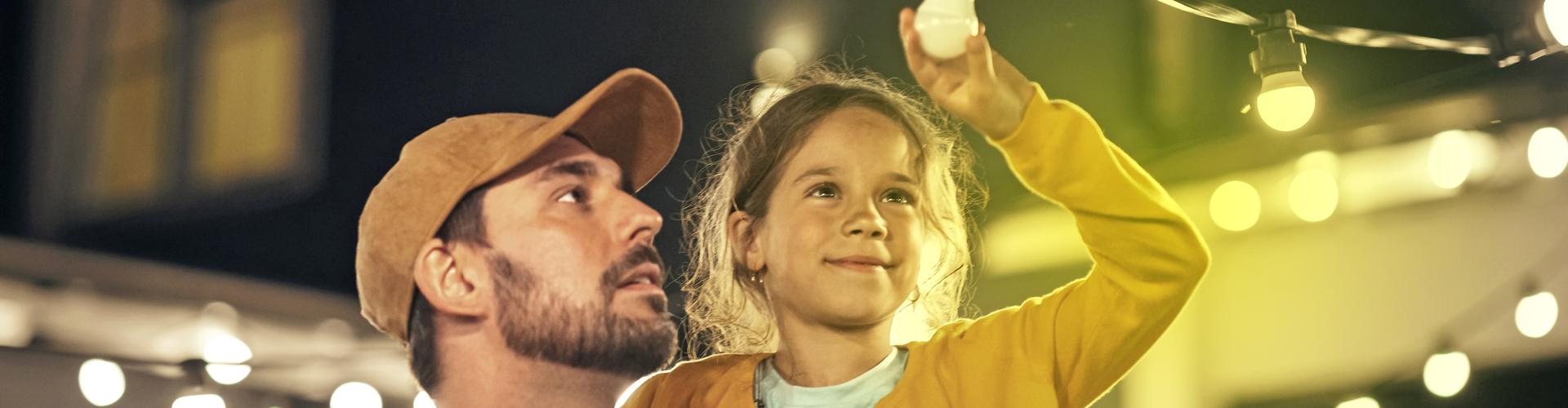 Ein Mann hat ein Mädchen auf dem Arm, das auf eine Lichterkette zeigt Ein Mann hat ein Mädchen auf dem Arm, das auf eine Lichterkette zeigt