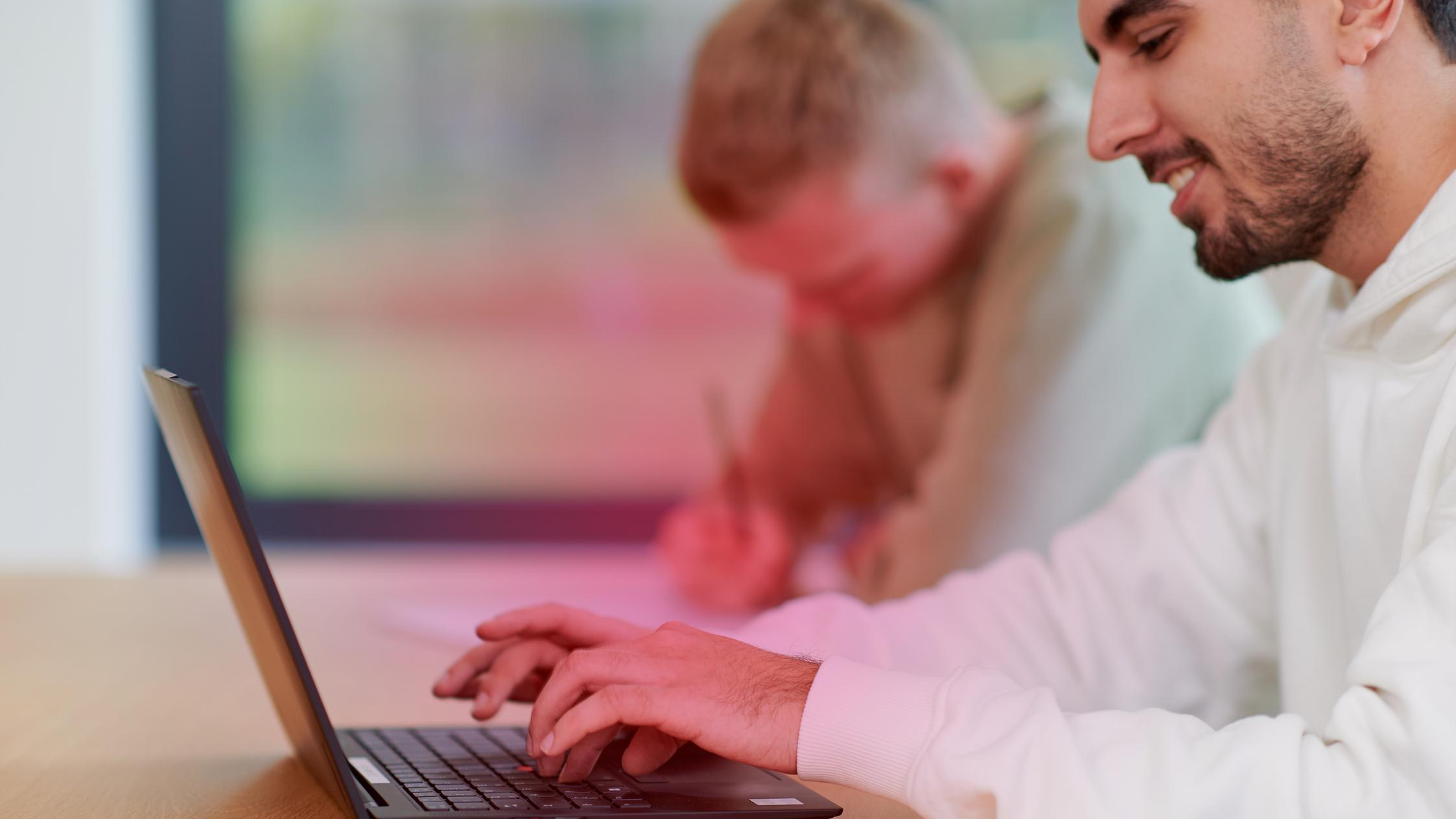 Zwei junge Männer sitzen an einem Schreibtisch und haben einen Laptop vor sich Zwei junge Männer sitzen an einem Schreibtisch und haben einen Laptop vor sich