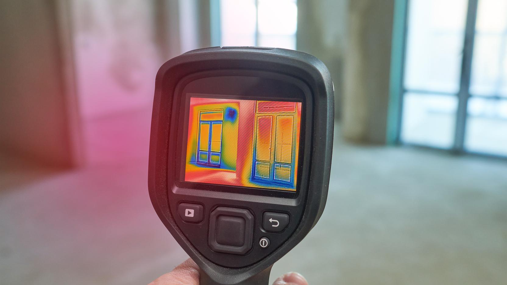 Eine Wärmebildkamera ist auf ein Haus gerichtet und zeigt Wärmeverluste Eine Wärmebildkamera ist auf ein Haus gerichtet und zeigt Wärmeverluste