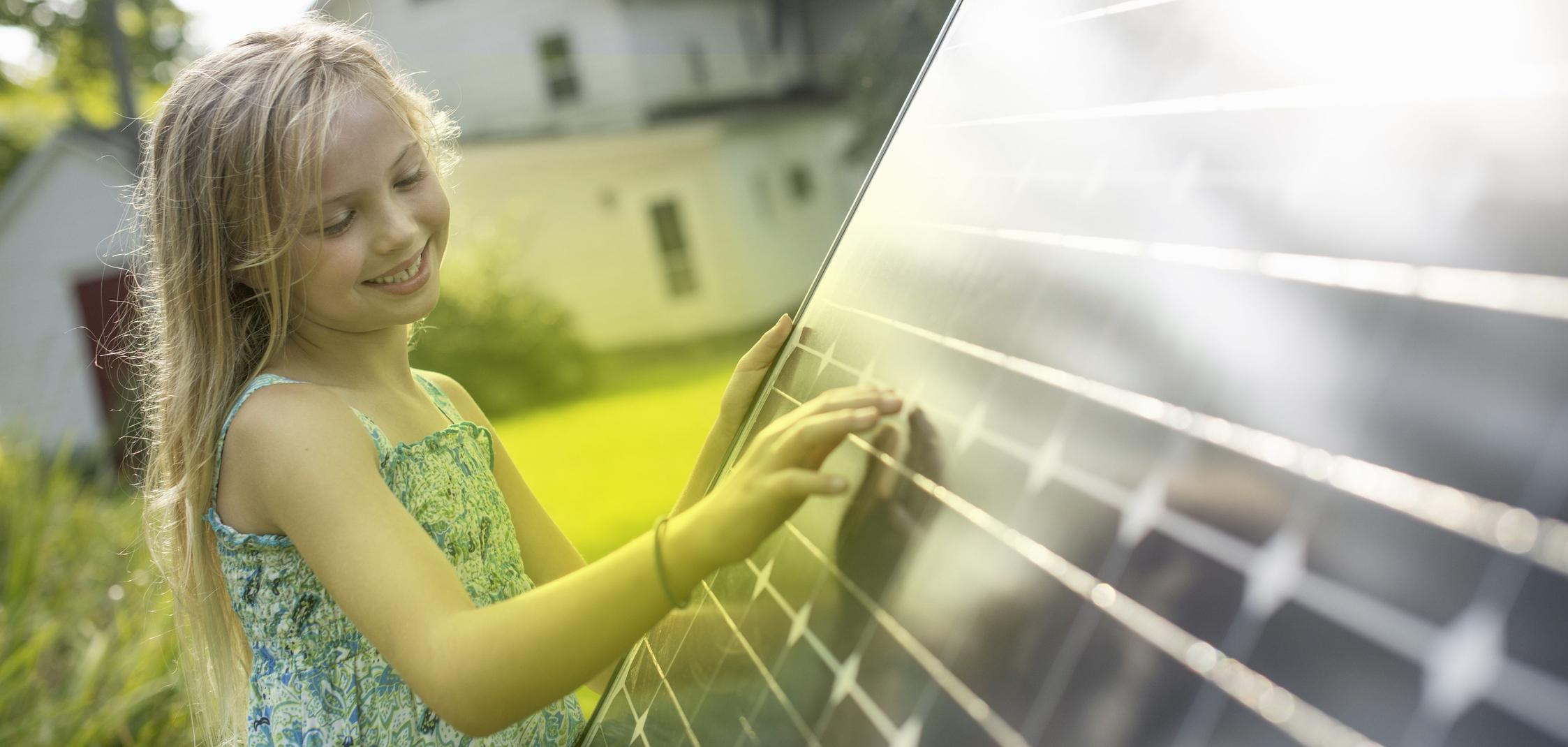 Ein Mädchen steht vor einem Photovoltaik-Modul und schaut es an Ein Mädchen steht vor einem Photovoltaik-Modul und schaut es an